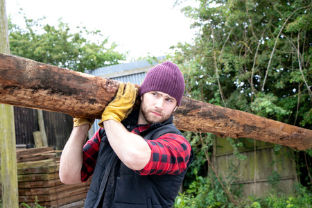 Handsome male lumberjack carries wood log on his shoulderの写真素材