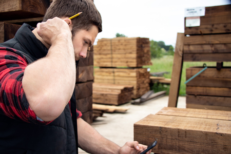 Lumber yard worker, carpenter at wood yard counts inventory with mobile deviceの写真素材