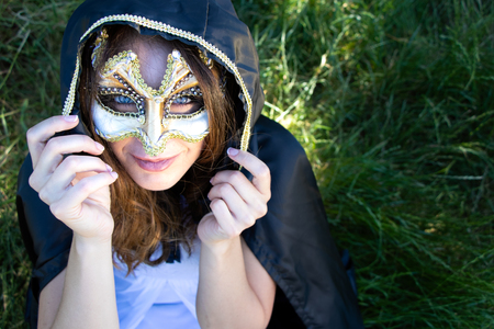 Beautiful woman with blue eyes, long brown hair and hood wears a mask as blue eyes look at the cameraの写真素材