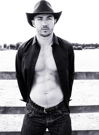 Sexy, handsome, hunky cowboy with hat open shirt and pecs looks at cameraの写真素材