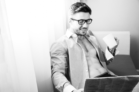 Handsome businessman, sits by hotel window reading newspaper and drinking coffeeの写真素材