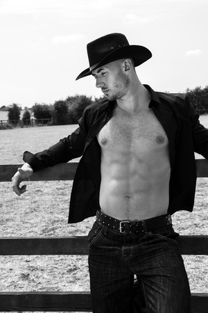 Sexy, handsome, hunky cowboy with hat open shirt and pecs looks away from cameraの写真素材