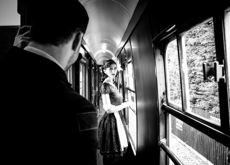 Beautiful woman dressed in red tea vintage tea dress on locomotive standing in corridor with officer watching herの写真素材