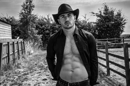Sexy, handsome, hunky cowboy with hat open shirt and sixpack abs looking at cameraの写真素材