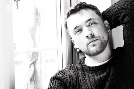 Portrait of handsome man with beard sitting in window