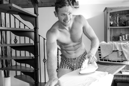 Shirtless fit guy with abs ironing clothes on ironing boardの写真素材