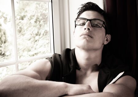 Portait of good looking young latino man with spectacles, sitting in windowの写真素材