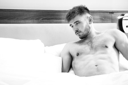 Good looking naked man lying in between white sheetsの写真素材