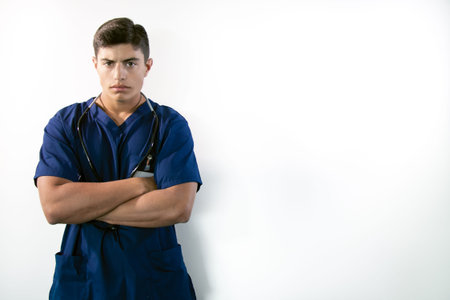 Handsome male doctor in blue scrubs with folded arms isolated against white backdrop