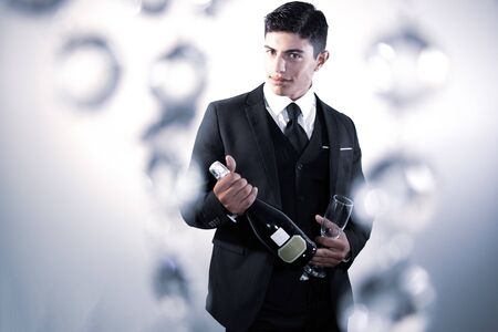 Good looking man in suit holding bottle of sparkling wine and glassの写真素材
