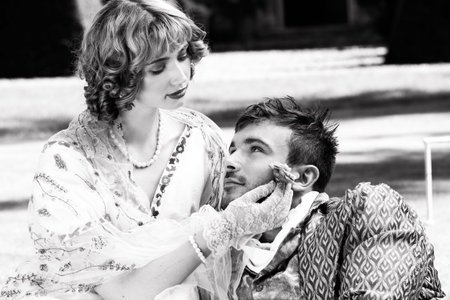 Young lovers dressed in vintage clothing. Man looking into partners eyes as she strokes his face...