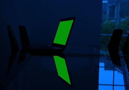 Laptop computer on glass desk in empty dark room with rain spattered window and green screen for own copy or graphicの写真素材