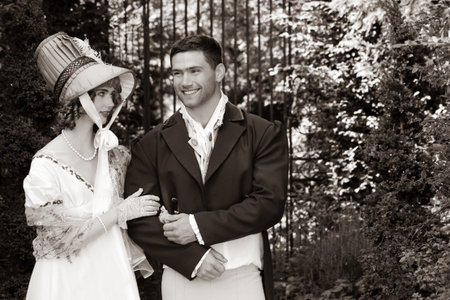 Potrait of young attractive couple dressed in vintage clothing walking through garden arm in arm,...