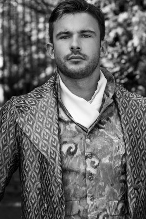 Portrait of handsome gentleman dressed in vintage costume standing in stately home courtyard with...