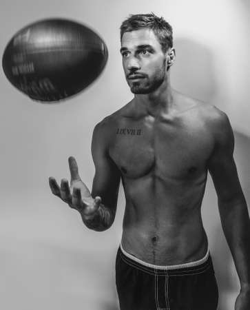 Black and white portrait of young attractive topless muscular man with beard tossing american footballの写真素材