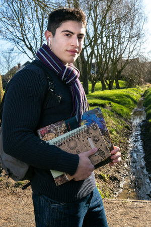 Handsome young teenage male student walking to school in sunshine, carrying books and rucksack