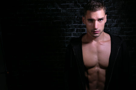 Portrait of handsome serious young man looking at camera with open black shirt revealing muscular...