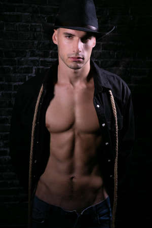 Portrait of handsome cowboy looking at camera wearing hat with open black shirt revealing defined pecs and sixpack absの写真素材