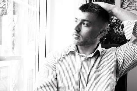 Portrait of handsome man with beard sitting in windowの写真素材