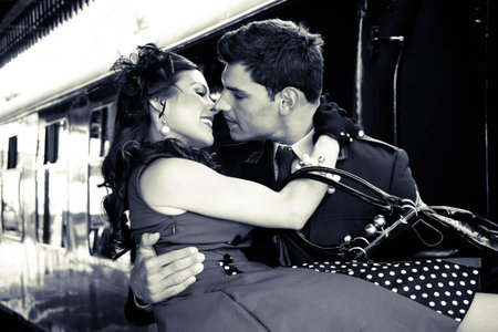 Vintage couple, man in uniform holds his sweetheart in his arms as they are about to kiss with train...
