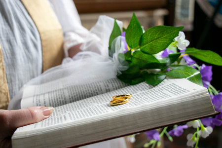Wedding gold rings on bible with flowers and part of vicar in backgroundの写真素材