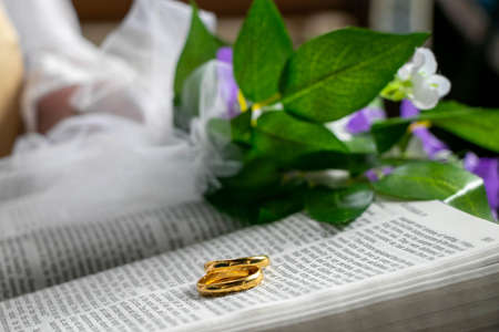 Wedding gold rings on bible with flowers and part of vicar in backgroundの写真素材