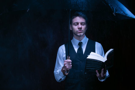 Man dressed in suit holding unbrella and reading bookの写真素材