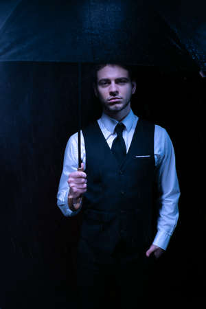 Man dressed in suit holding unbrella and looking at camera at night timeの写真素材
