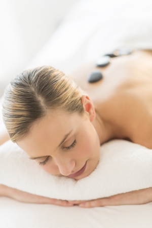 Relaxed young woman getting hot stone therapy at health spaの写真素材