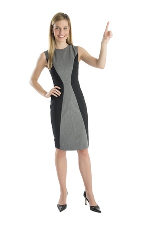 Full length portrait of happy businesswoman with hand on hip pointing upwards against white backgroundの写真素材