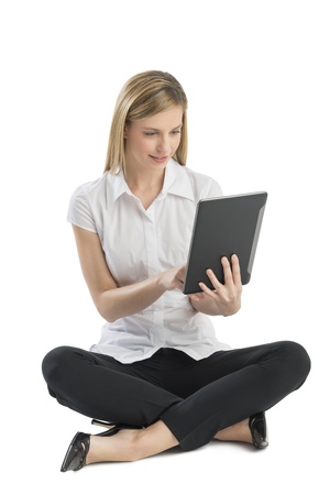 Full length of young businesswoman using digital tablet while sitting on floor against white backgroundの写真素材