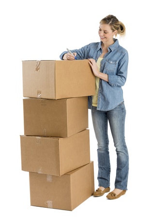 Full length of happy young woman writing on stacked cardboard boxes against white backgroundの写真素材