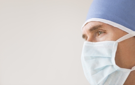 Close-up of male surgeon wearing surgical mask and cap looking away against gray backgroundの写真素材