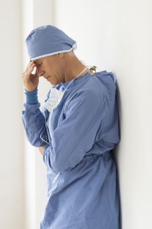 Side view of tensed male surgeon with head in hands standing in hospitalの写真素材