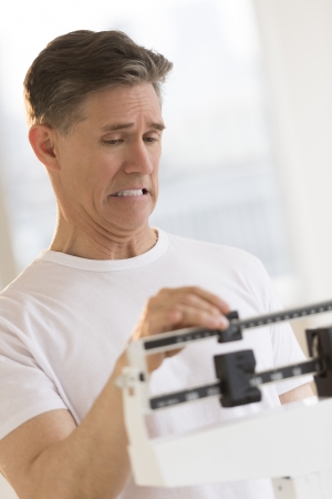 Mature man clenching teeth while using balance weight scale at health clubの写真素材