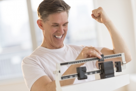 Excited mature man clenching fist while using balance weight scale at gymの写真素材