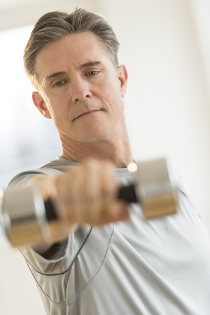 Front view of mature man lifting dumbbell at gymの写真素材