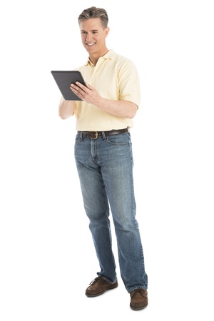 Happy mature man using digital tablet while standing isolated over white backgroundの写真素材