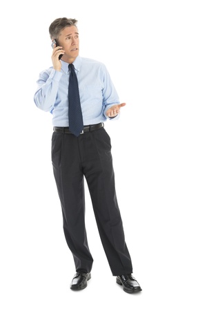 Full length of mature businessman gesturing while using smart phone against white backgroundの写真素材