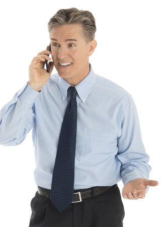 Happy mature businessman gesturing while answering smart phone against white backgroundの写真素材