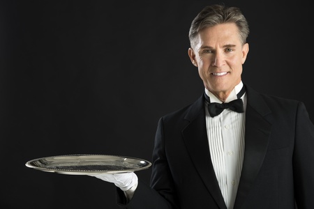 Portrait of confident waiter carrying serving tray isolated over black backgroundの写真素材
