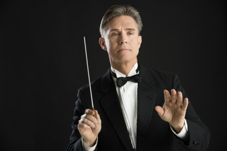 Confident mature male orchestra conductor directing with his baton against black backgroundの写真素材