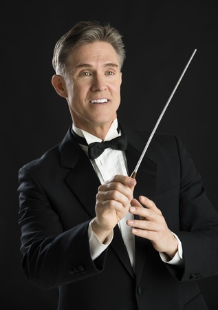Mature male music conductor smiling while directing with his baton isolated on black backgroundの写真素材