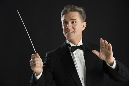 Mature male orchestra conductor looking away while directing with his baton against black backgroundの写真素材
