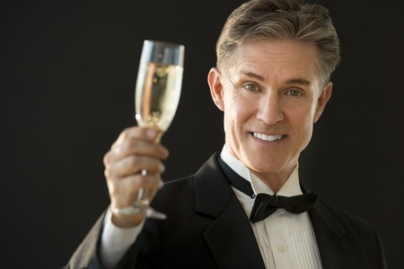 Portrait of happy mature man in tuxedo holding champagne flute against black backgroundの写真素材