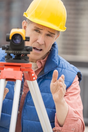 Mature cartographer gesturing while using theodolite at construction siteの写真素材
