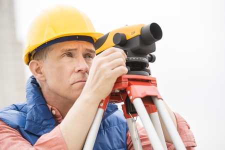 Mature surveyor measuring distances through theodolite at construction siteの写真素材