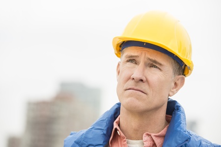 Close-up of tired manual worker wearing hardhat looking away at construction siteの写真素材