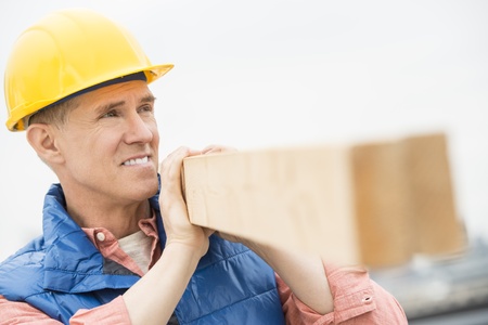 Close-up of construction worker looking away while carrying wooden plankの写真素材