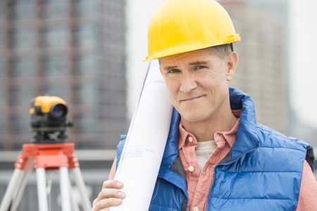 Portrait of confident male architect holding rolled up blueprint at construction siteの写真素材